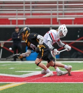 Two youth lacrosse players compete for possession of the ball on a field, showcasing athletic movement and teamwork.