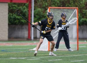 High school lacrosse players in action on a field, focused on a game during rainy weather.