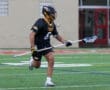 Lacrosse player wearing a black jersey runs with a stick on a field, showcasing athleticism and team spirit.