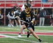 Lacrosse player in a black Tigers jersey dodges an opponent on the field during a rainy game.
