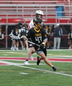 Lacrosse player in a black Tigers jersey dodges an opponent on the field during a rainy game.