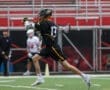 A young lacrosse player in a black uniform sprints with a stick, showcasing agility on the field.