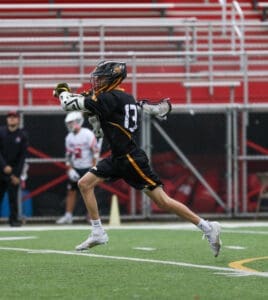 A young lacrosse player in a black uniform sprints with a stick, showcasing agility on the field.