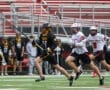 Players in lacrosse uniforms compete on the field, showcasing athleticism and teamwork during an intense match.