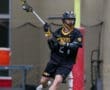 Lacrosse player in black jersey passes the ball during a game on a turf field, showcasing athleticism and teamwork.