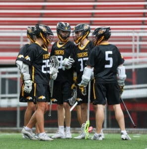 Lacrosse team huddled together in black and yellow uniforms, discussing strategy on the field.