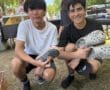 Two young men smiling and posing with colorful Crocs at an outdoor event, surrounded by greenery and people.