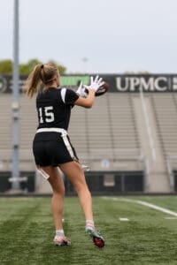 Female football player wearing jersey #15 catches a pass on a field, showcasing her agility and skill in action.