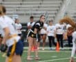 Female football player in action on the field, focused with teammates in the background during a game practice.