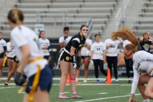 Female football player in action on the field, focused with teammates in the background during a game practice.