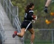 A female athlete in action, running with a football during a game on a grassy field.
