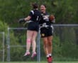 Two female athletes joyfully celebrate after a play during a flag football game on a grassy field.