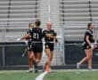Girls' flag football team celebrating on the field, showcasing teamwork and sportsmanship in athletic gear.