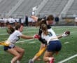 Two female athletes engage in a fierce game of flag football, with one player attempting to evade a tackle while holding the ball.