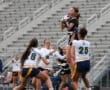 Girl catching a football during a competitive flag football game, with teammates in action on a field.