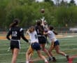 Girls competing in flag football, with players reaching for a pass while a referee oversees the game.