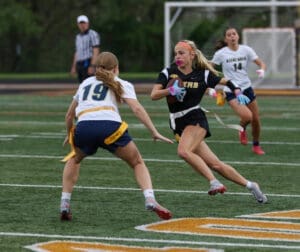 Girls' flag football game action, with one player sprinting past an opponent on the field, showcasing competitive spirit.