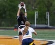 A female athlete catches a football while another player prepares to defend during a flag football game outdoors.