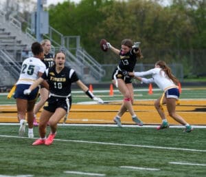 Exciting moment in girls' flag football game, player leaps to catch a pass while being defended by an opponent.