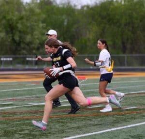Female athlete running with a football during a flag football game, showcasing agility and teamwork on the field.