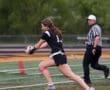 Girl running with a football during a game, with a referee in the background on a sports field.