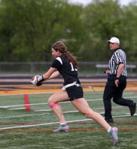 Girl running with a football during a game, with a referee in the background on a sports field.