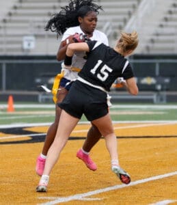 Two female athletes compete in a flag football game, showcasing dynamic action on the field.
