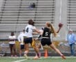 Girl in black sports uniform throws football while being defended by an opponent in a women's flag football game.