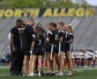 Girls' flag football team in black uniforms huddles with a coach on the field at North Allegheny High School.