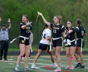 High school girls' flag football team in action, signaling plays on the field during a game.