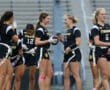 Girl's flag football team in black jerseys smiles and prepares for a game, showcasing teamwork and athletic spirit.