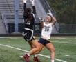 Two female players compete for a football during a game, showcasing athleticism on the field at dusk.