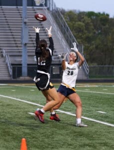 Two female players compete for a football during a game, showcasing athleticism on the field at dusk.