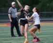 Female flag football player throws a pass while being defended by an opponent during a game, with an official observing.