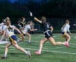 Female athletes compete in a flag football game, showcasing teamwork and athleticism on the field under evening lights.