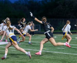 Female athletes compete in a flag football game, showcasing teamwork and athleticism on the field under evening lights.