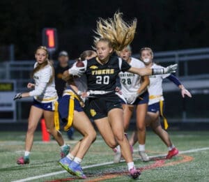 Girls' flag football game: player #20 from the Tigers dodges opponents while running with the ball under stadium lights.