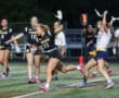 Female athletes competing in a night flag football game, with player #20 advancing the ball on the field.
