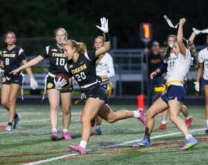 Female athletes competing in a night flag football game, with player #20 advancing the ball on the field.