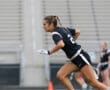 A young female athlete sprinting on the field, wearing a black uniform with number 2 during a flag football game.