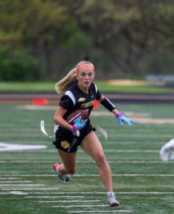 Girl in black Tigers uniform running with a football on a field, showcasing athleticism and focus during a game.
