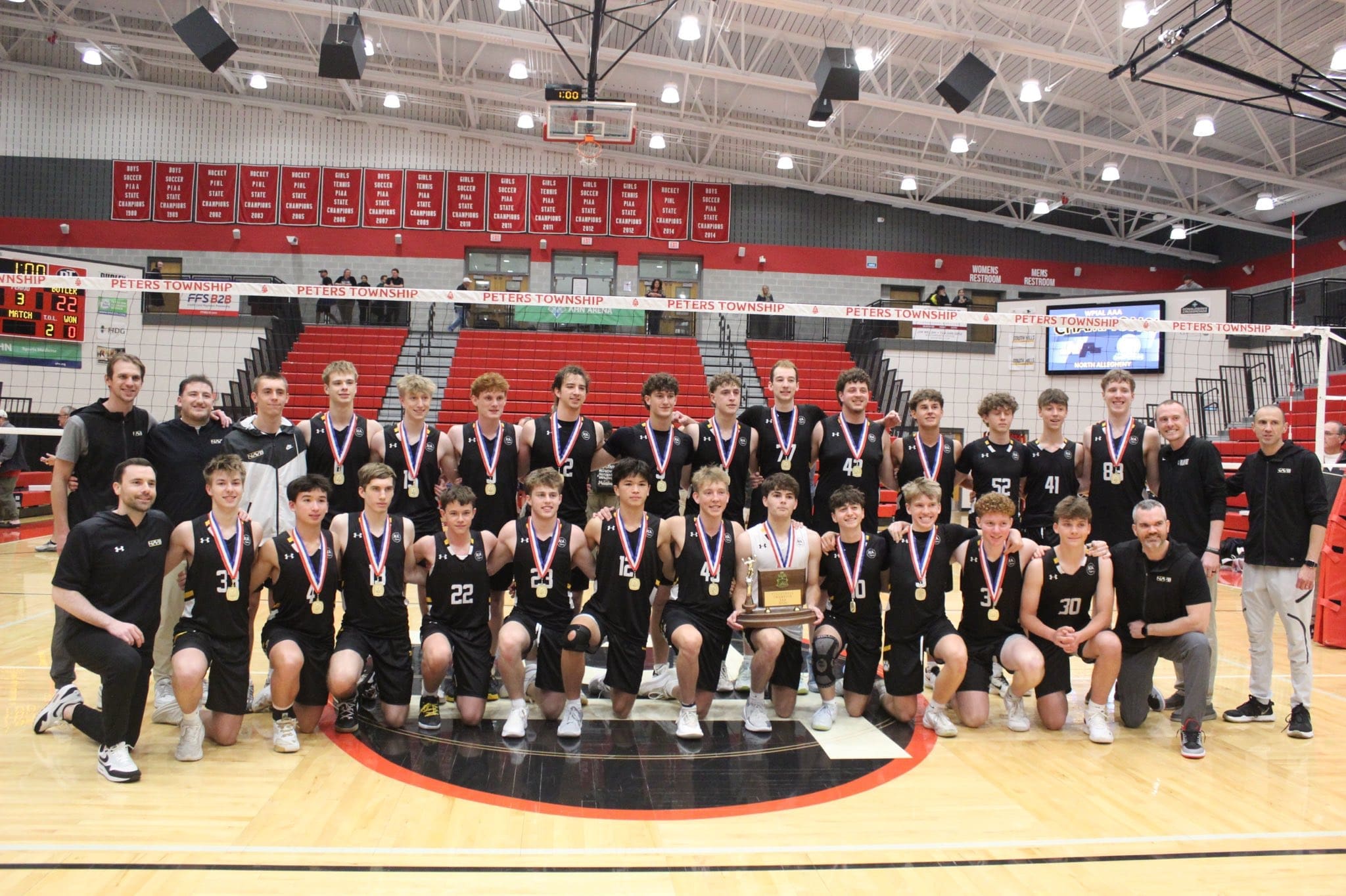 Championship-winning youth volleyball team poses with medals and trophy after a successful match at Peters Township.