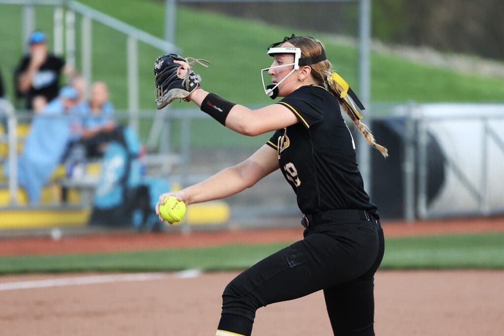 A female softball pitcher in action, preparing to throw a fastball during a game on a sunny day.