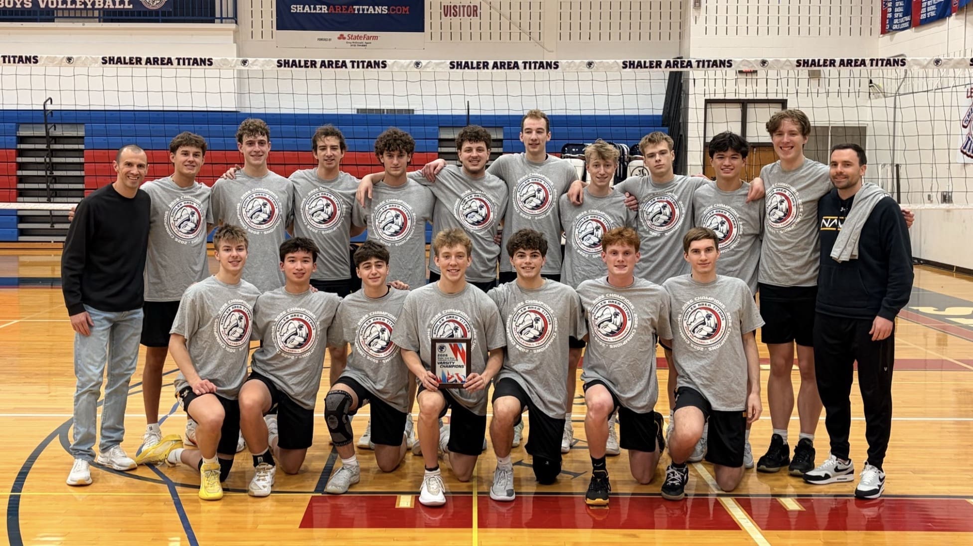 Shaler Area Titans boys volleyball team celebrates a championship win, posing with their trophy in the gym.