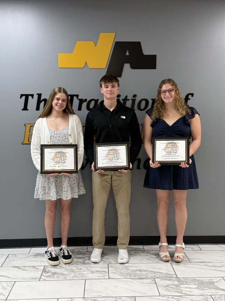 Three students proudly display their scholarship awards against a branded backdrop at a recognition event.