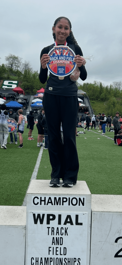 Young athlete celebrating on a podium after winning the WPIAL Track and Field Championships with a medal.