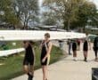 Young rowers carry a boat at a bustling regatta, showcasing teamwork and athletic spirit on a sunny day.