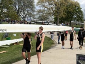 Young rowers carry a boat at a bustling regatta, showcasing teamwork and athletic spirit on a sunny day.