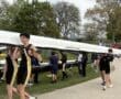 Rowers carrying a boat at a competition, showcasing teamwork and athleticism on a sunny day.