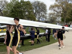 Rowers carrying a boat at a competition, showcasing teamwork and athleticism on a sunny day.